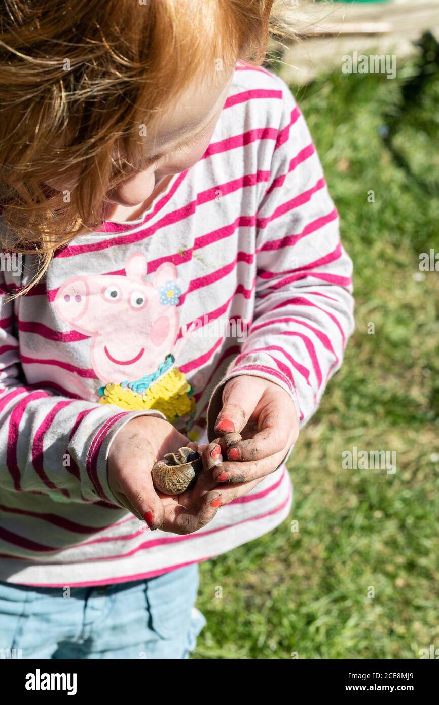 Un tout-petit à tête rouge jouant avec un escargot dans un jardin par elle-même. Banque D'Images