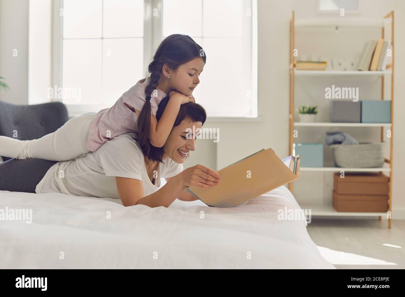 Fille heureuse couché sur les jeunes mères dans la chambre et lire le livre ensemble Banque D'Images