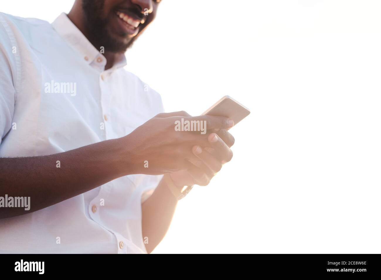 Vue ci-dessous de l'homme barbu noir en chemise blanche avec smartphone tout en communiquant avec vos amis en ligne Banque D'Images