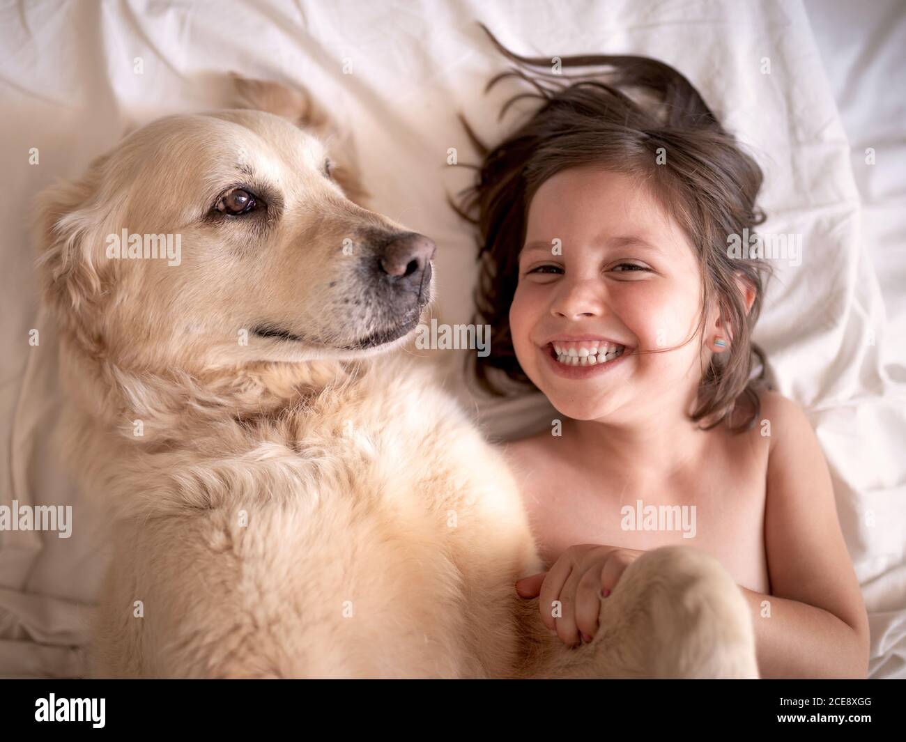 Vue de dessus de gaie enfant reposant sur le lit avec adorable Hovawart et regarder l'appareil photo à la maison Banque D'Images