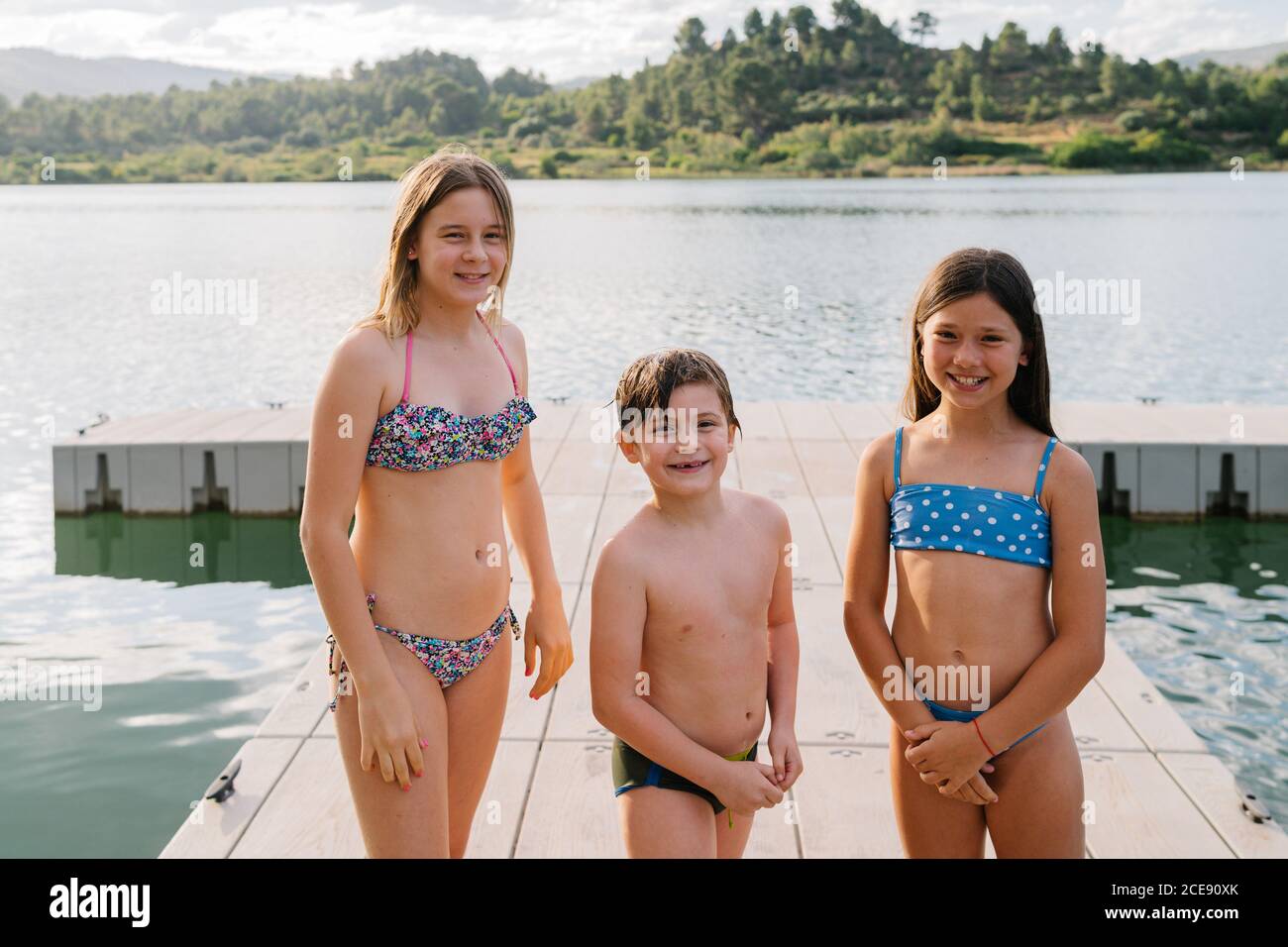 Frère et sœurs souriants en maillot de bain debout sur le quai près lac et  regarder l'appareil photo tout en appréciant les vacances d'été Photo Stock  - Alamy