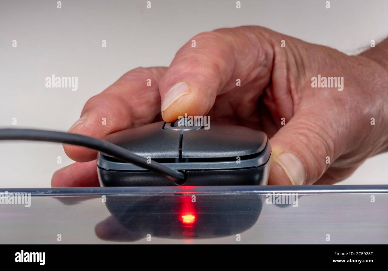 Gros plan de la main d’un homme à l’aide d’une souris d’ordinateur (périphérique d’entrée), avec molette de défilement, en gris / gris, sur une surface transparente. Banque D'Images