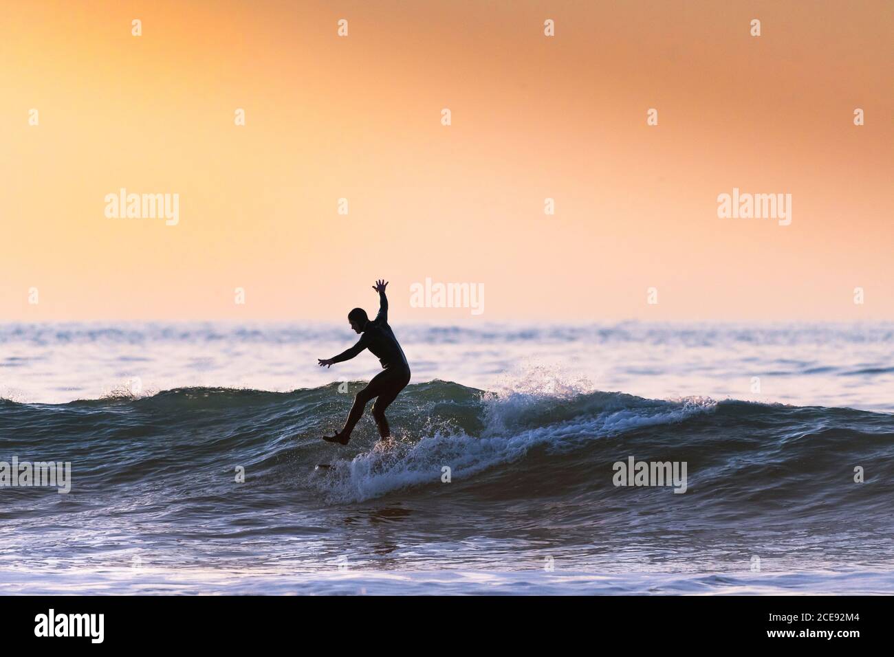 Un surfeur qui monte une vague et se tient sur une jambe en soirée à Fistral, à Newquay, en Cornwall. Banque D'Images