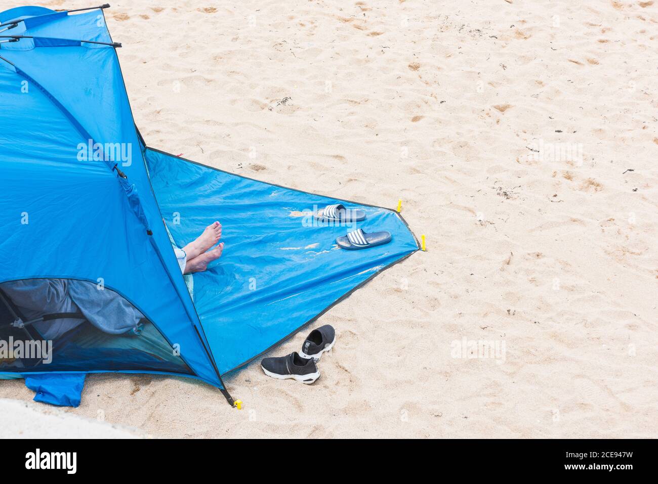 Un holidaymaker assis à l'intérieur d'un abri de plage bleu sur la plage de Fistral à Newquay, en Cornouailles. Banque D'Images