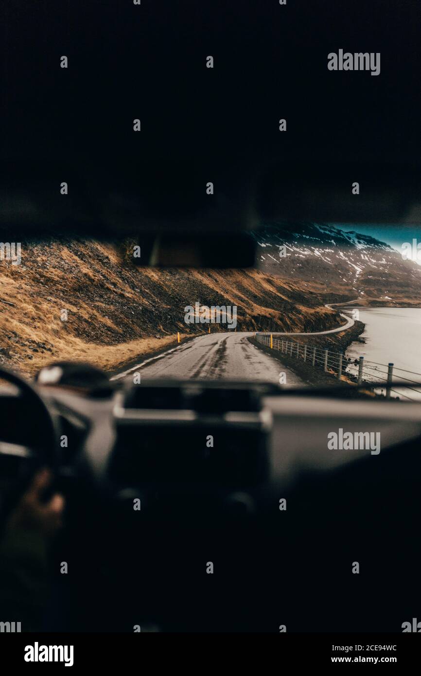 Vue prise de la voiture à travers l'écran du vent de longue route longeant la mer grise et les rochers, l'Islande. Banque D'Images