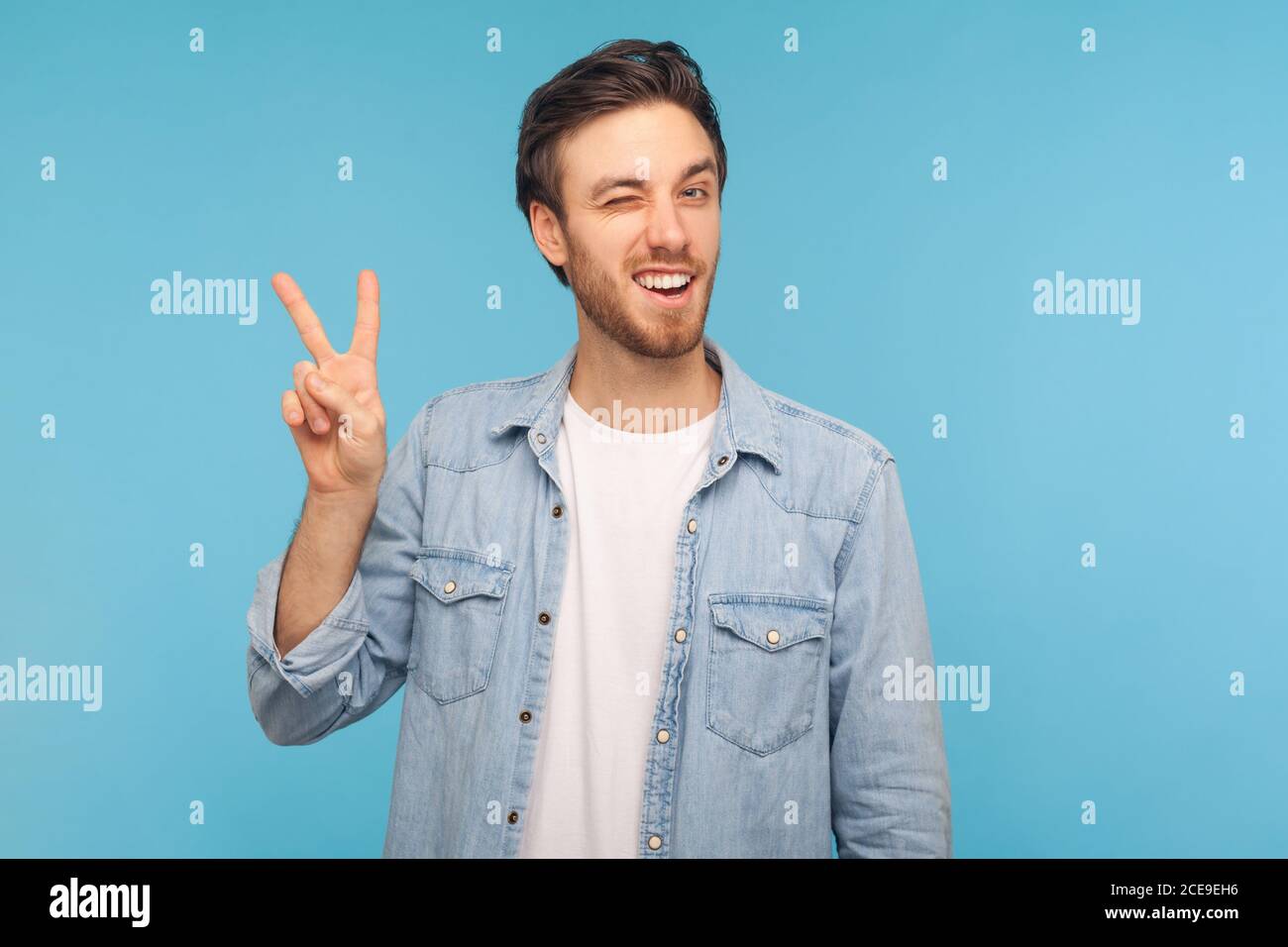 Je gagne ! Portrait de l'homme heureux optimiste dans le travailleur maillot denim faisant le geste de la victoire et wencing playentilly à l'appareil photo, montrant la paix, signe de v avec double Banque D'Images