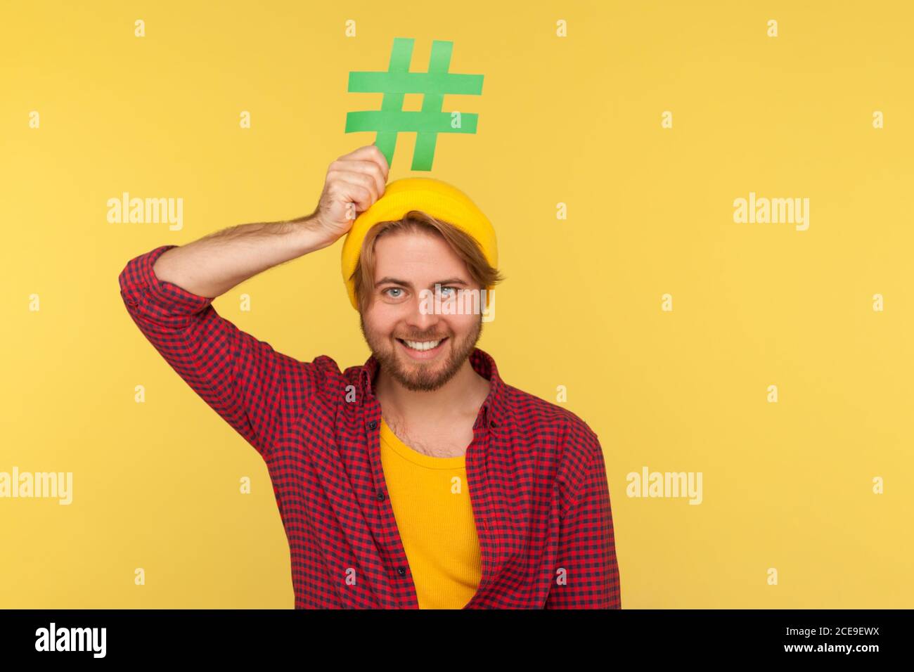 Hashtag, tendances Internet. Happy Funny hipster mec dans une chemise à carreaux souriant et tenant le signe de hash sur la tête, symbole du réseau social de message viral. Banque D'Images