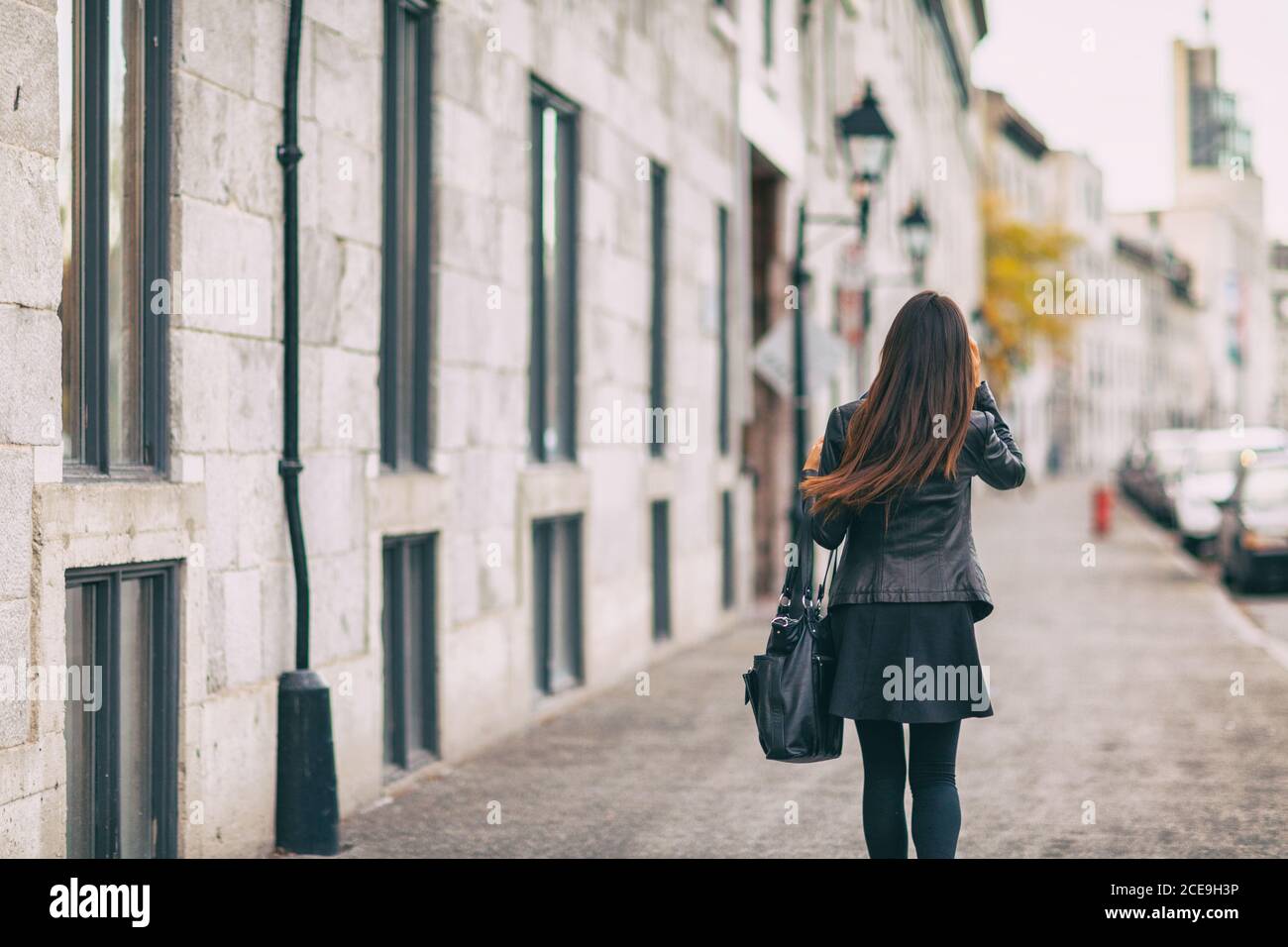 Ville Street style de vie les gens se déplacer jeune femme de derrière marcher dehors dans les couleurs d'automne portant une veste en cuir et une jupe noire, de longs cheveux bruns Banque D'Images