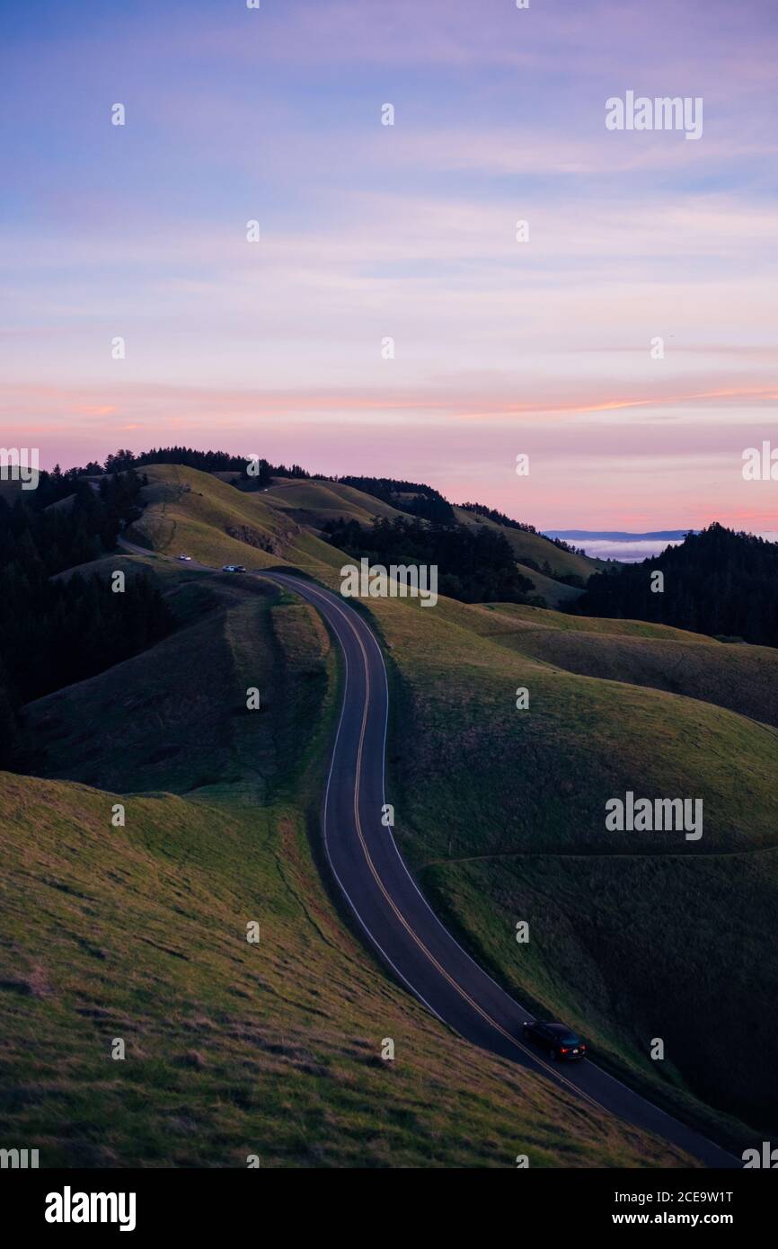 Circulation matinale sur la route à flanc de colline contre le ciel pastel dans la campagne californienne. CopySpace. Banque D'Images