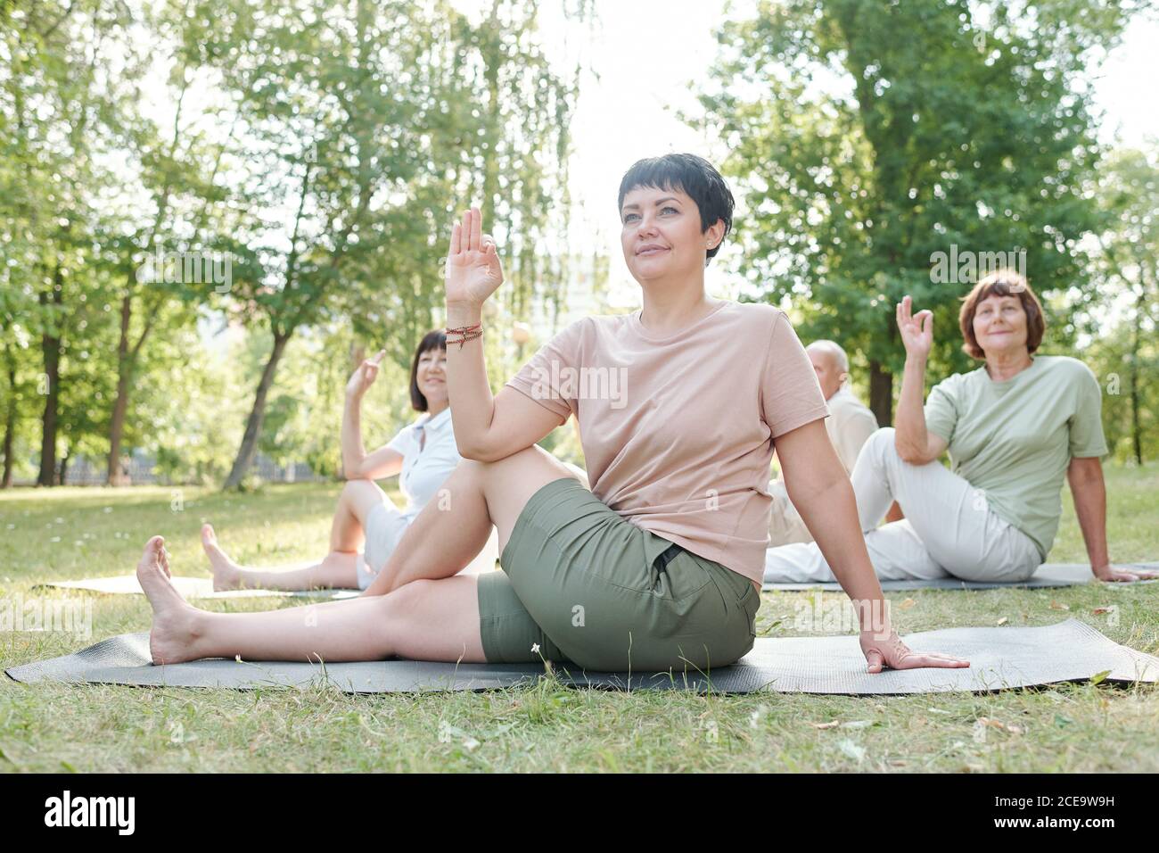 Entraîneur de yoga attrayant avec les cheveux courts assis sur le tapis et pratiquer la pose de marichis avec des étudiants en classe de groupe Banque D'Images