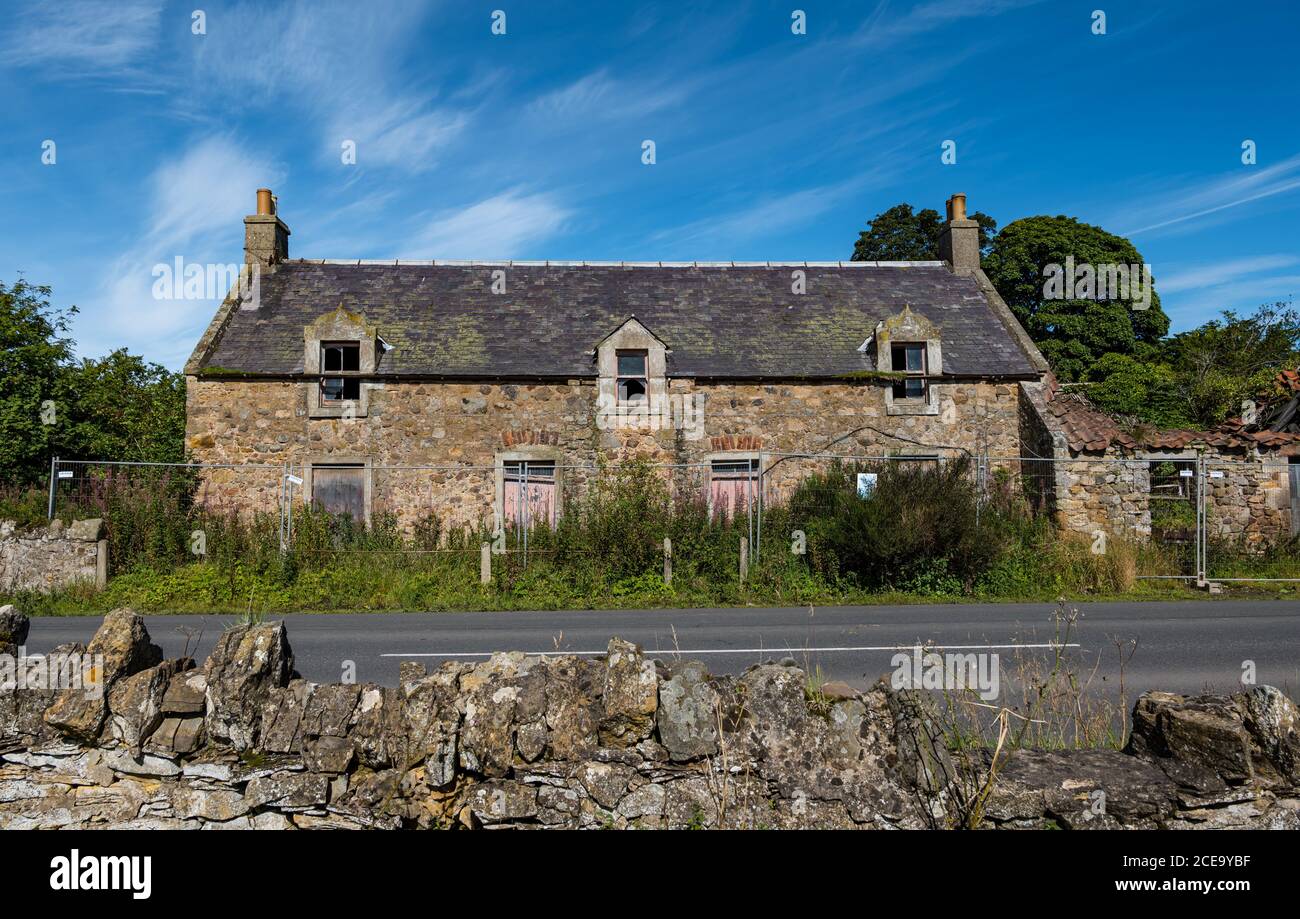 Des bâtiments agricoles abandonnés avec des fenêtres cassées et une barrière au bord de la route, Peaston, East Lothian, Écosse, Royaume-Uni Banque D'Images