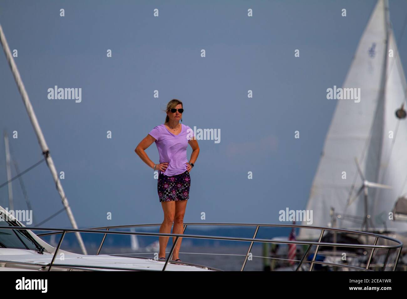 Annapolis, MD 08/21/2020: Une femme blonde et attirante dans ses années quarante portant un chemisier et une jupe lilas est debout sur le pont d'un yacht avec ses mains sur Banque D'Images