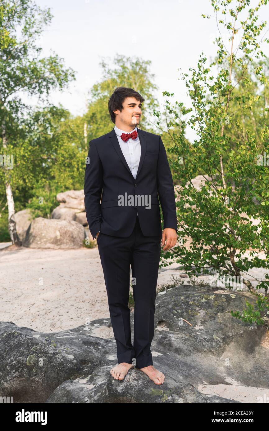 Jeune homme souriant pieds nus vêtu d'un costume noir avec noeud papillon  rouge et sur le rocher du bord de mer, à l'écart des rêves Photo Stock -  Alamy