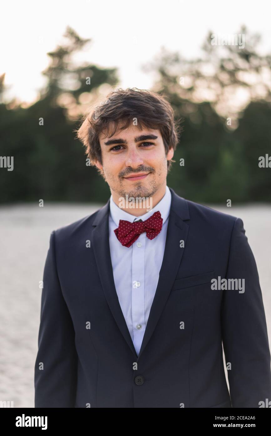 Homme adulte portant un élégant costume noir avec noeud papillon et se  tenir sur la plage avec les mains dans les poches en regardant l'appareil  photo Photo Stock - Alamy