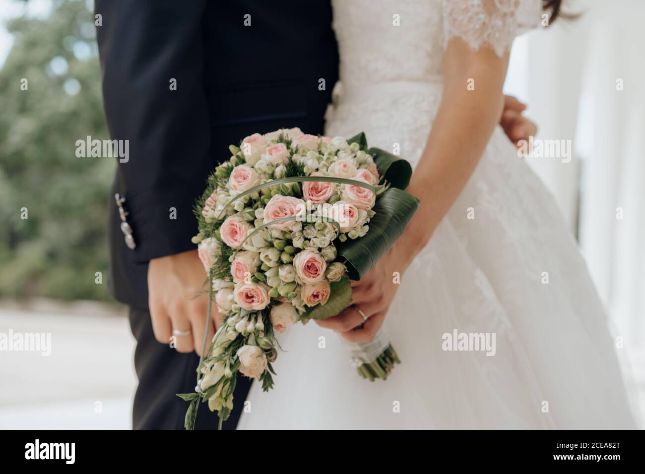 Vue de côté rognée de la mariée tenant un bouquet rose et baiser avec le marié à l'extérieur Banque D'Images