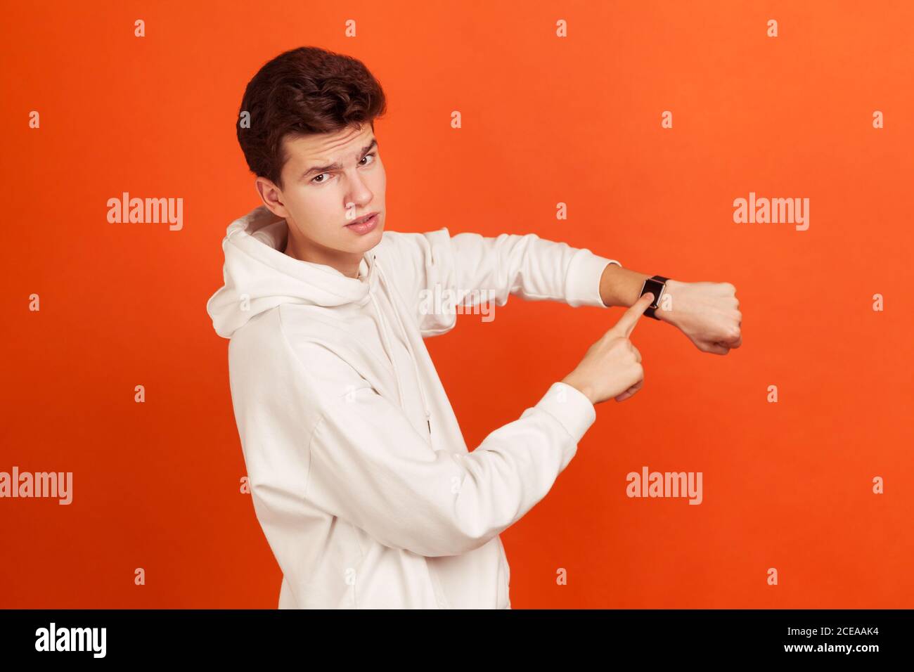 Jeune homme impatient dans un élégant sweat-shirt blanc avec le visage sérieux pointant son doigt sur la montre à main, temps d'agir, échéance. Prise de vue en studio isolée Banque D'Images