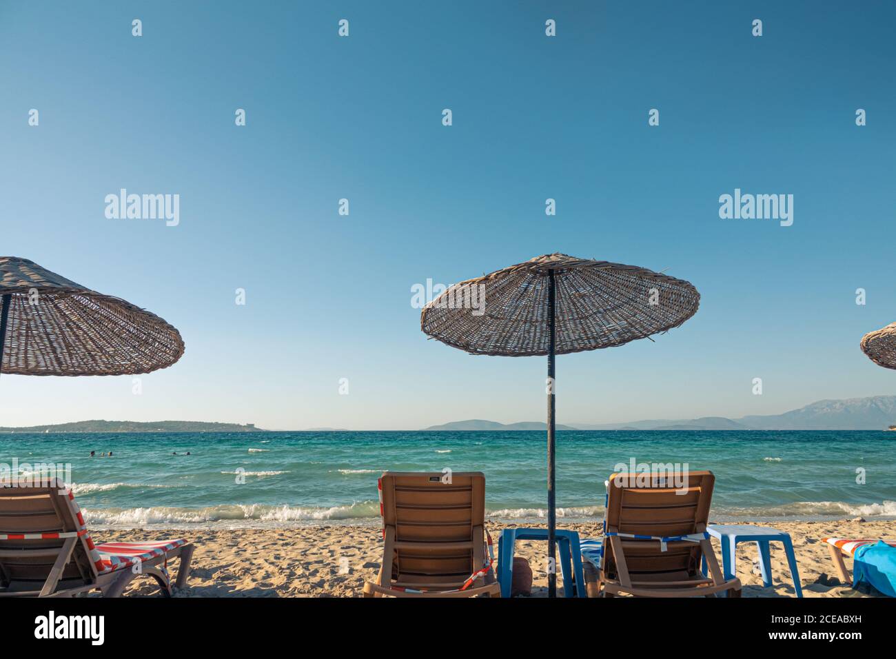 Plage de sable à Çeşme avec des parasols en paille et chaises longues comme arrière-plan très agréable. Banque D'Images