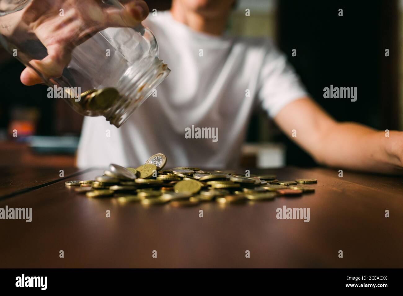 un jeune homme anonyme a versé de petites pièces de monnaie dans un pot en verre plan d'examen en bois Banque D'Images