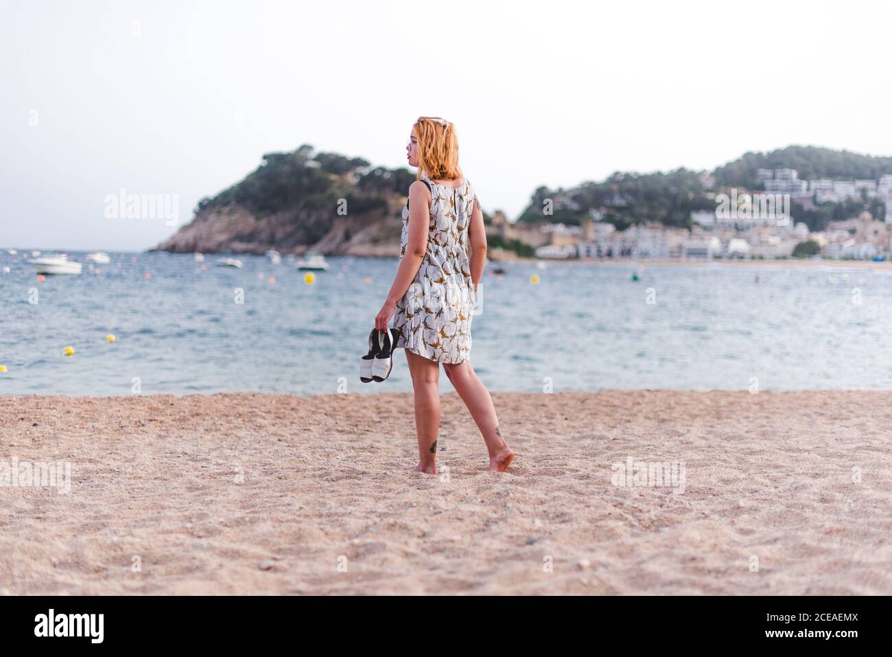 Vue latérale d'une petite femme portant des sandales tout en marchant sur une plage de sable à l'océan Banque D'Images