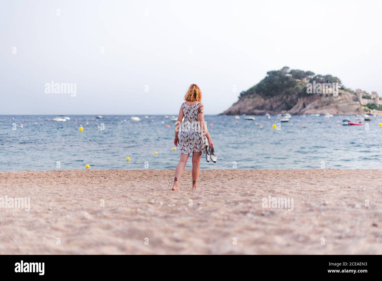 Vue latérale d'une petite femme portant des sandales tout en marchant sur une plage de sable à l'océan Banque D'Images