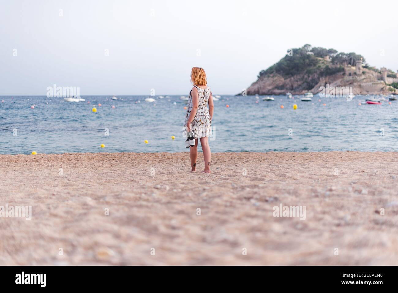Vue latérale d'une petite femme portant des sandales tout en marchant sur une plage de sable à l'océan Banque D'Images