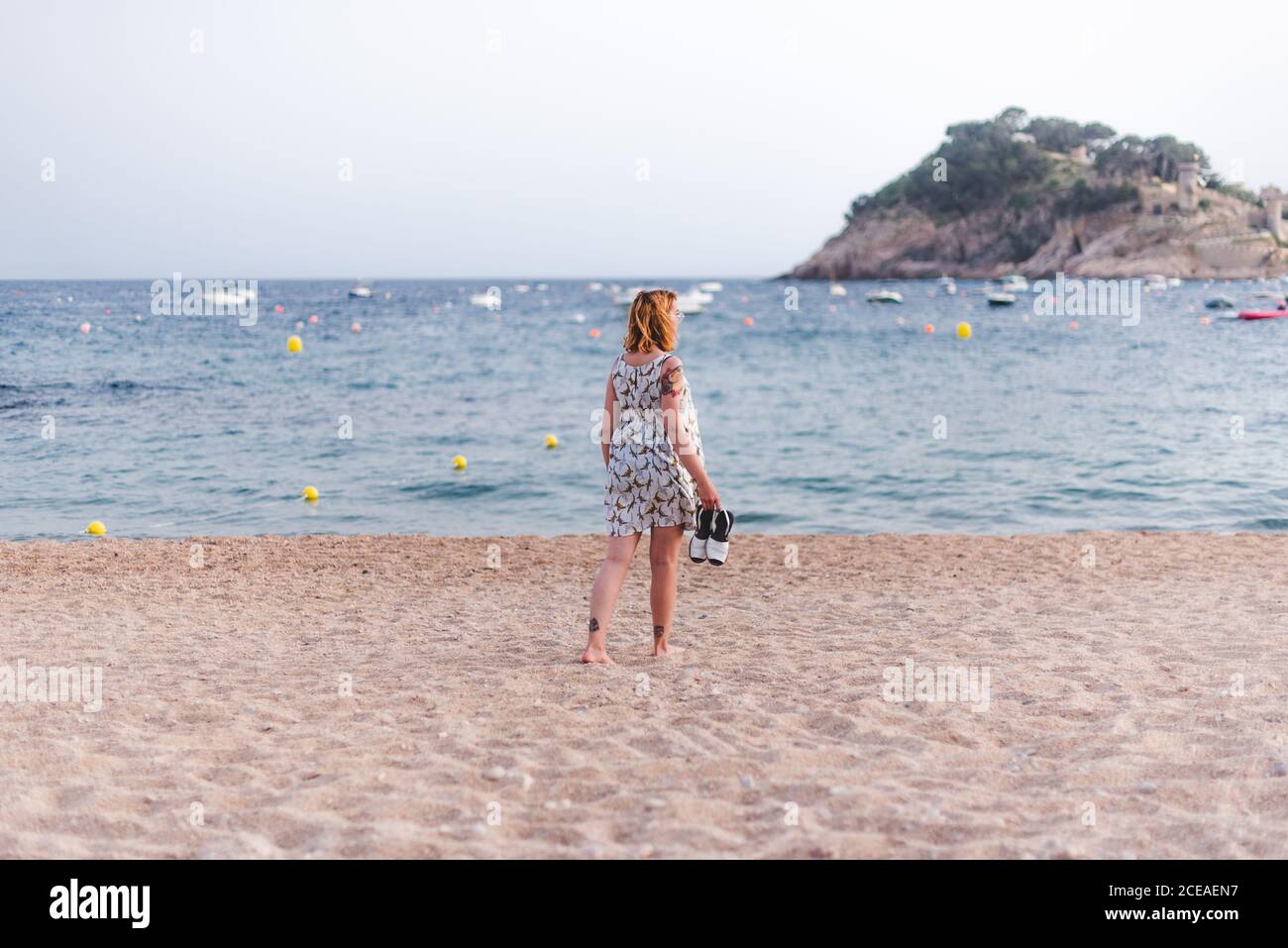 Vue latérale d'une petite femme portant des sandales tout en marchant sur une plage de sable à l'océan Banque D'Images