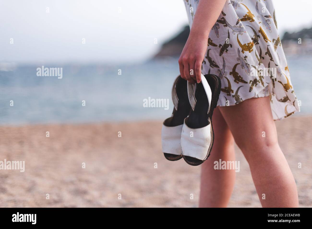 Vue latérale d'une petite femme portant des sandales tout en marchant sur une plage de sable à l'océan Banque D'Images