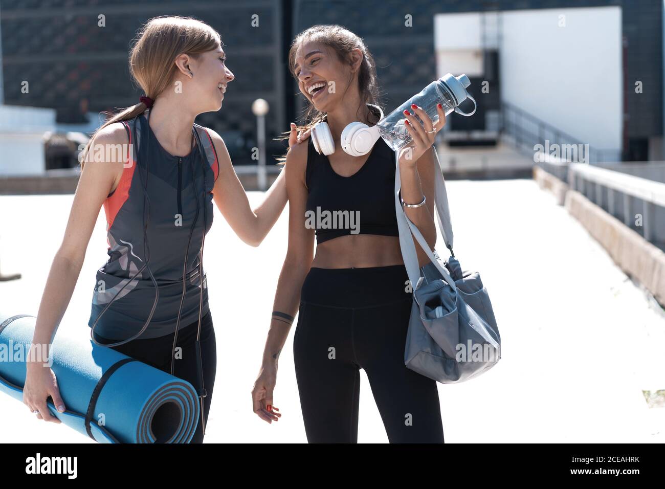 Deux jeunes femmes athlétiques souriantes qui marchent ensemble à l'extérieur après un entraînement sportif, qui parlent et s'embrasent les unes les autres. Banque D'Images