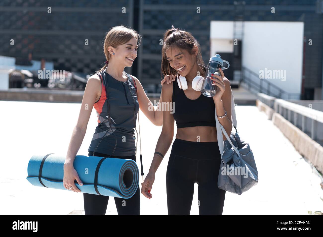 Deux jeunes femmes athlétiques souriantes qui marchent ensemble à l'extérieur après un entraînement sportif, qui parlent et s'embrasent les unes les autres. Banque D'Images