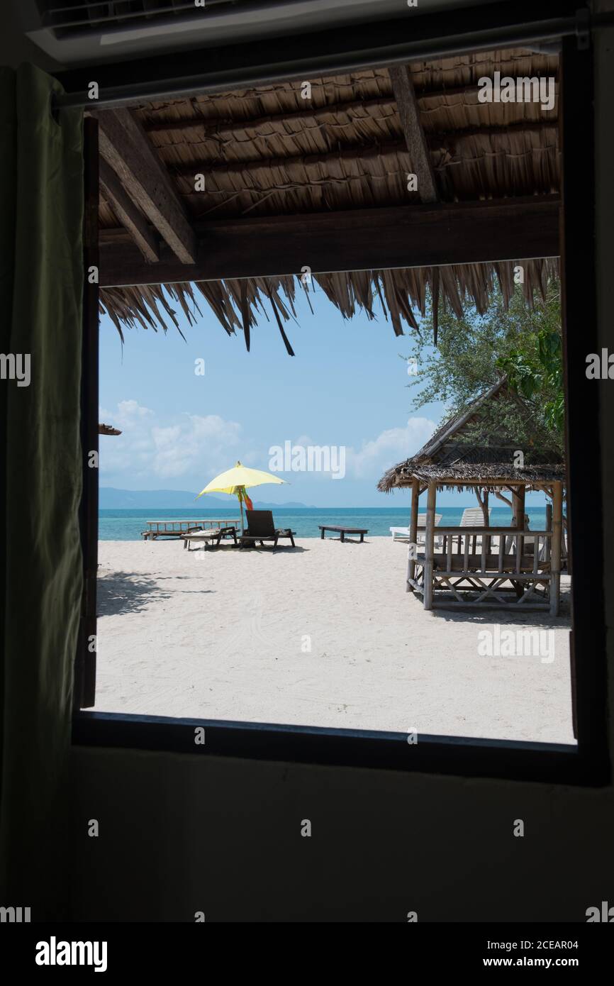 Vue de la fenêtre à la plage de sable avec des chaises longues et l'océan bleu sur l'île de Koh Phangan, en Thaïlande. Banque D'Images