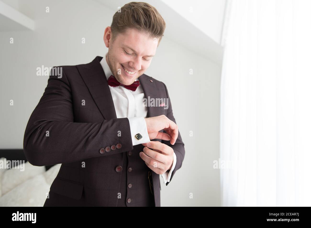 Vue d'en dessous du jeune homme souriant debout dans la chambre avec murs blancs et costume de mise Banque D'Images