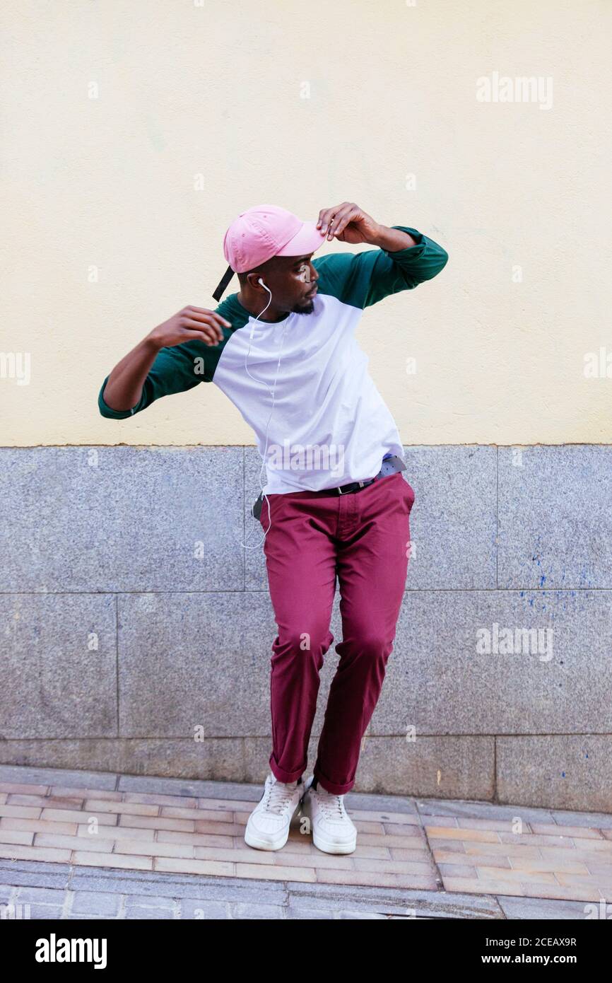 Homme blanc avec chemise verte et pantalon rouge avec rose casquette et  baskets dansant avec un casque sur fond de mur de rue Photo Stock - Alamy