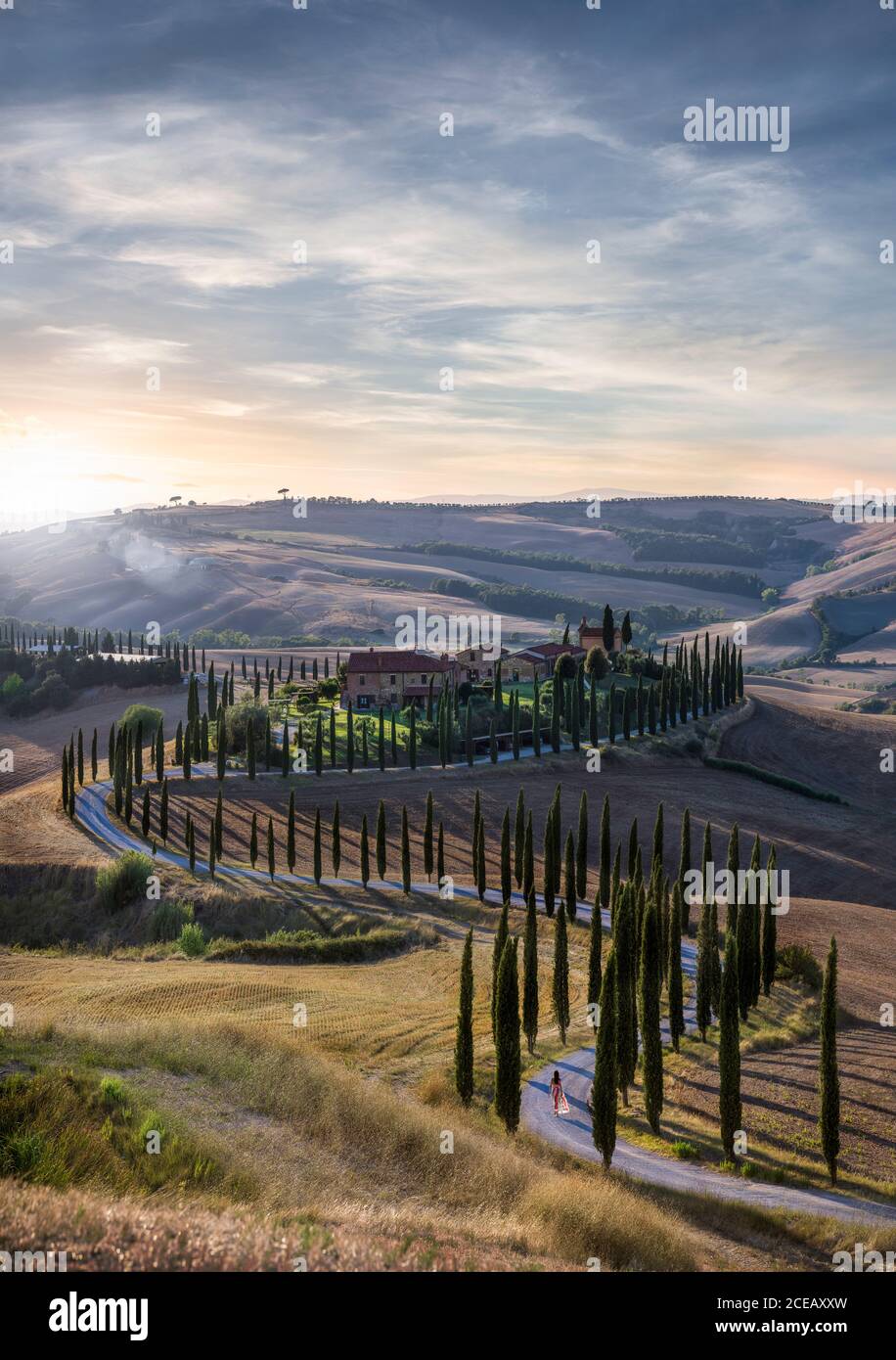 Coucher de soleil sur la belle route courbe de S en Toscane, Italie - femme en robe rouge à pied dans la distance Banque D'Images