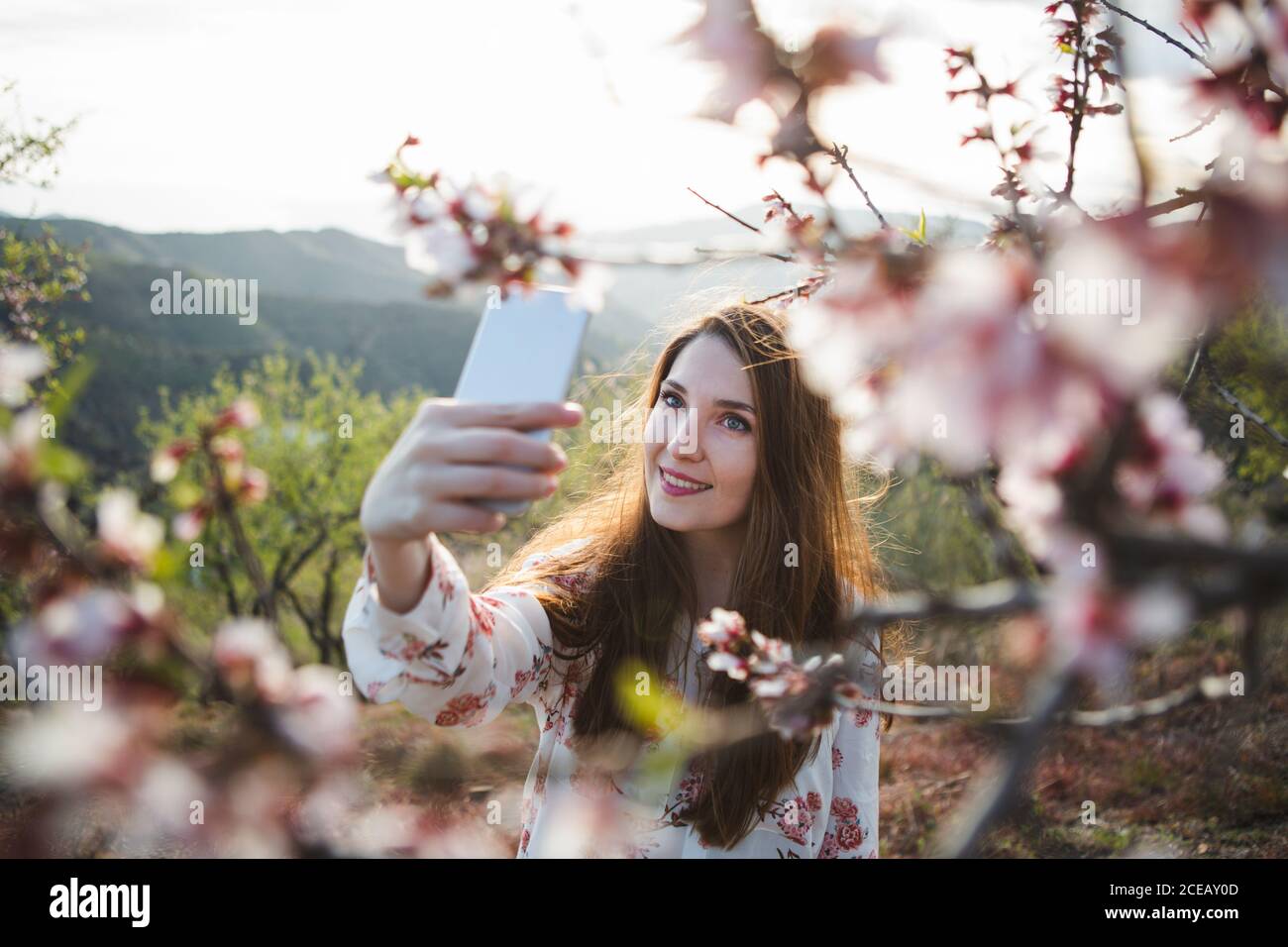 Dame gaie attrayant en tenant le téléphone mobile selfies près de blooming woods dans la montagne sur le jardin Banque D'Images