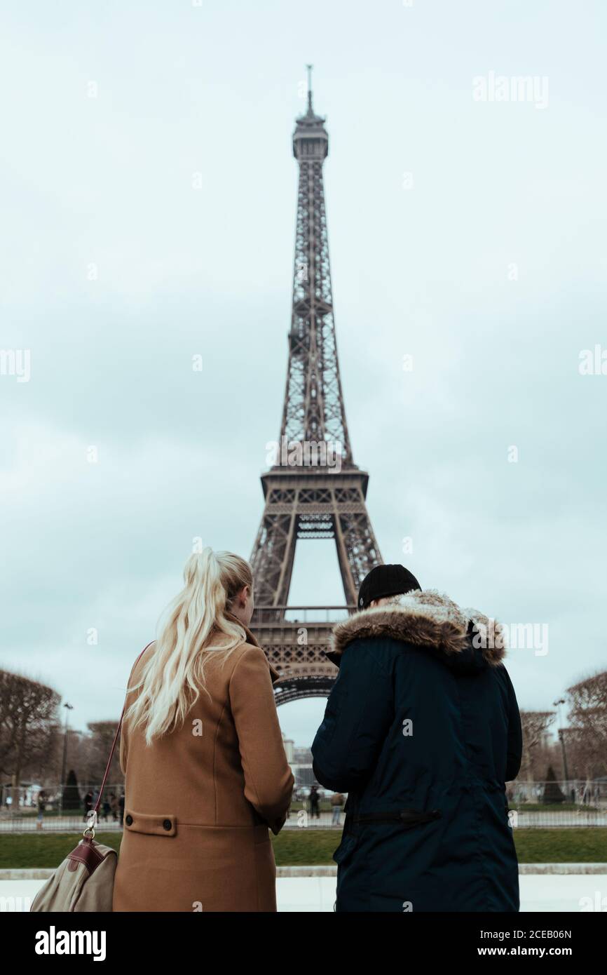 Vue arrière d'un couple debout à la tour Eiffel par temps nuageux à Paris, France. Banque D'Images