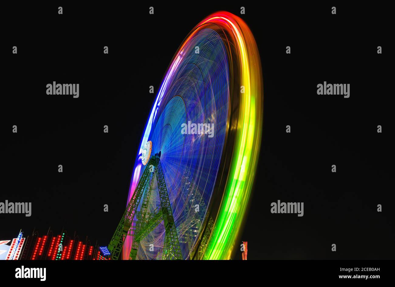 Traces de lumières colorées sur la grande roue en mouvement sur fond de ciel sombre de nuit. Banque D'Images