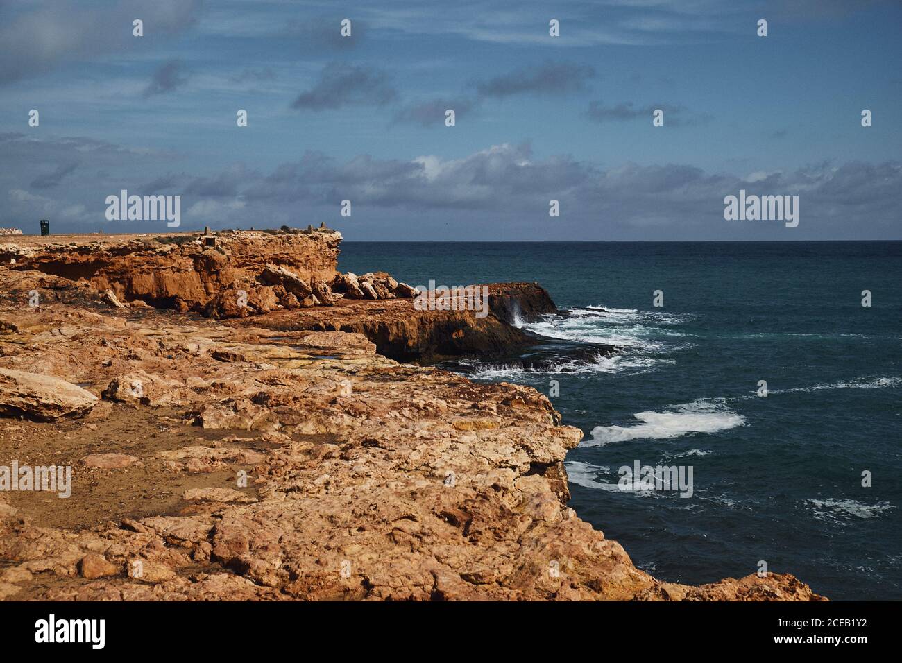 Côte rocheuse lavée par la mer mousseuse bleue sur fond de ciel avec nuages Banque D'Images