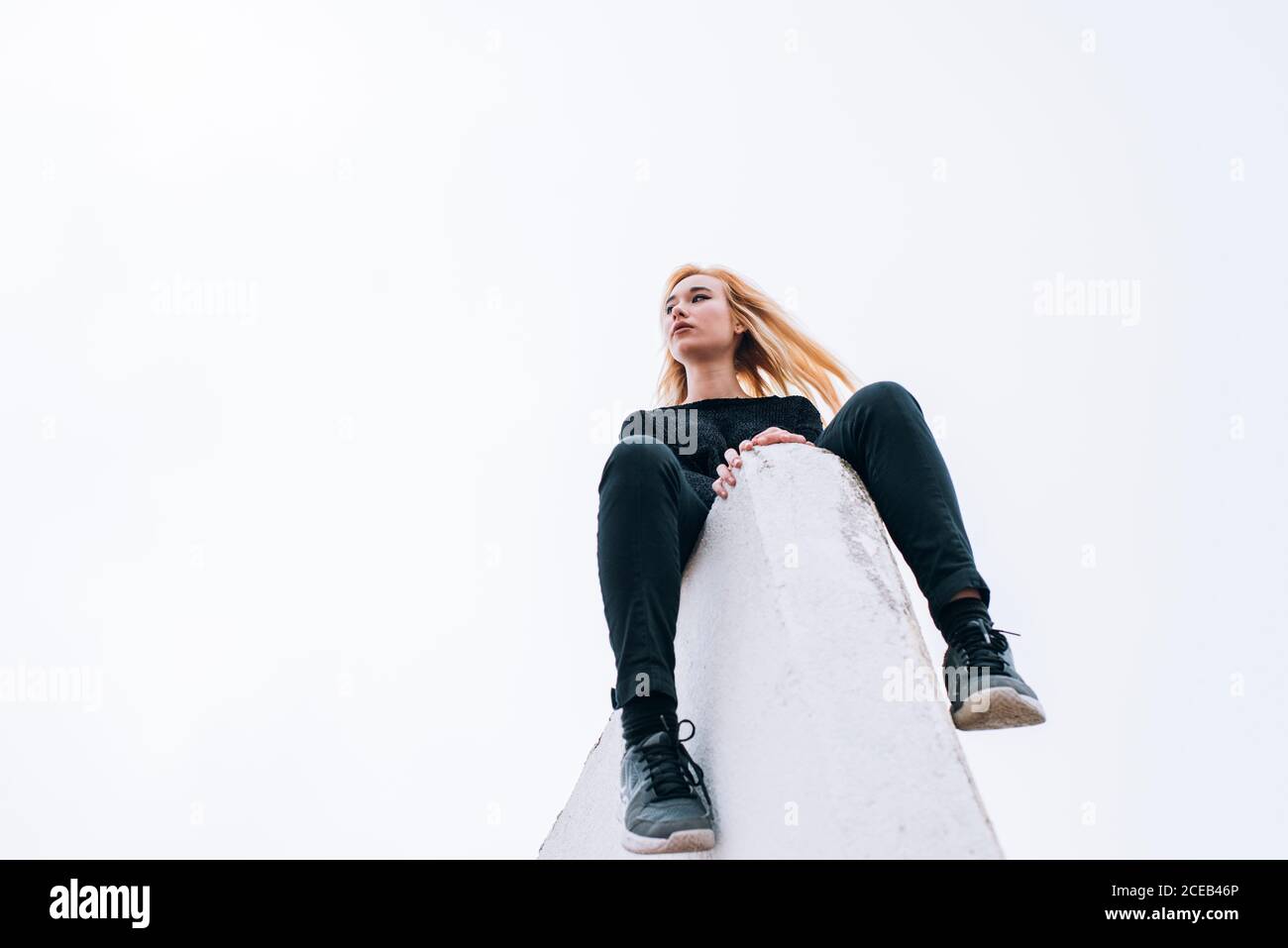 D'en-dessous, femme blonde assise sur le bord du toit sur fond de ciel gris. Banque D'Images