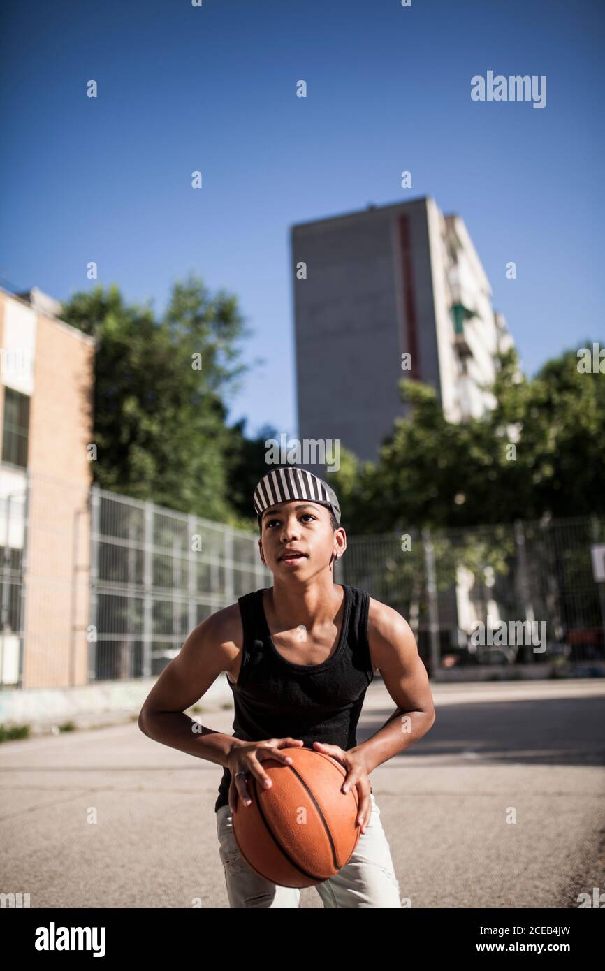 un jeune garçon afro avec chapeau joue au basket-ball sur le terrain de son quartier Banque D'Images