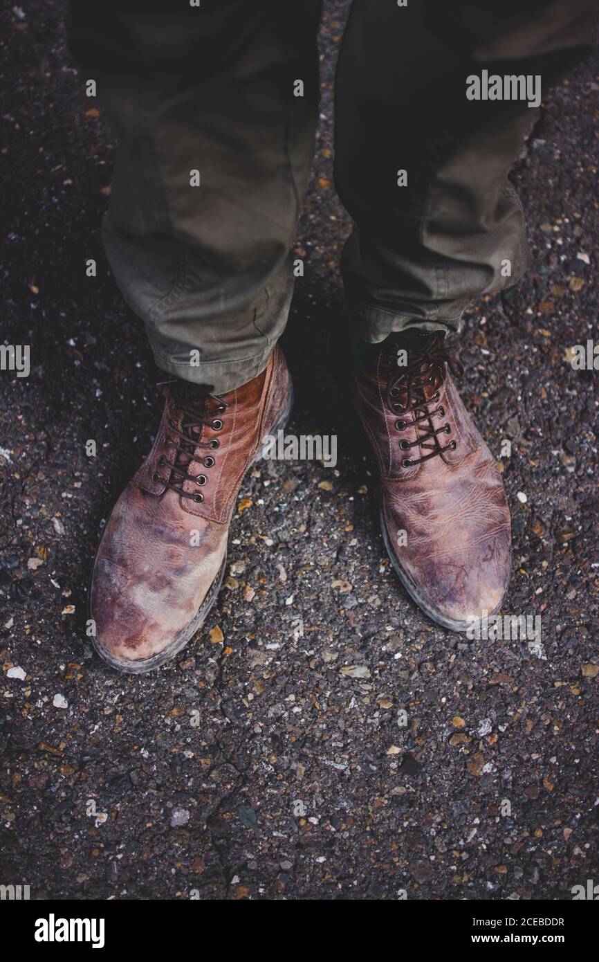 De ci-dessus, photo de jambes de voyageur anonyme dans sale bottes sur asphalte Banque D'Images