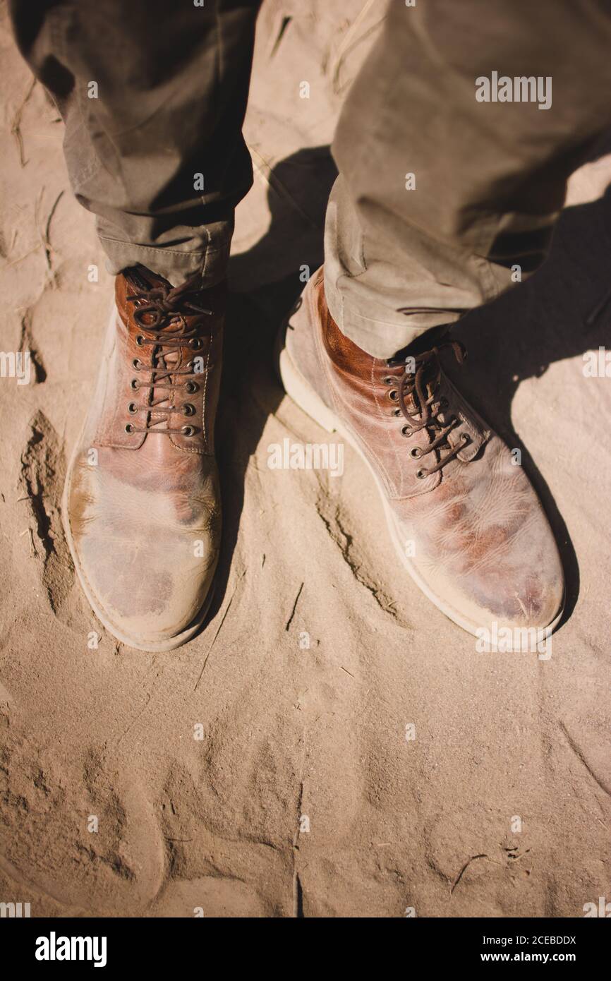 De ci-dessus, photo de jambes de voyageur anonyme dans sale bottes sur sol sablonneux sec Banque D'Images