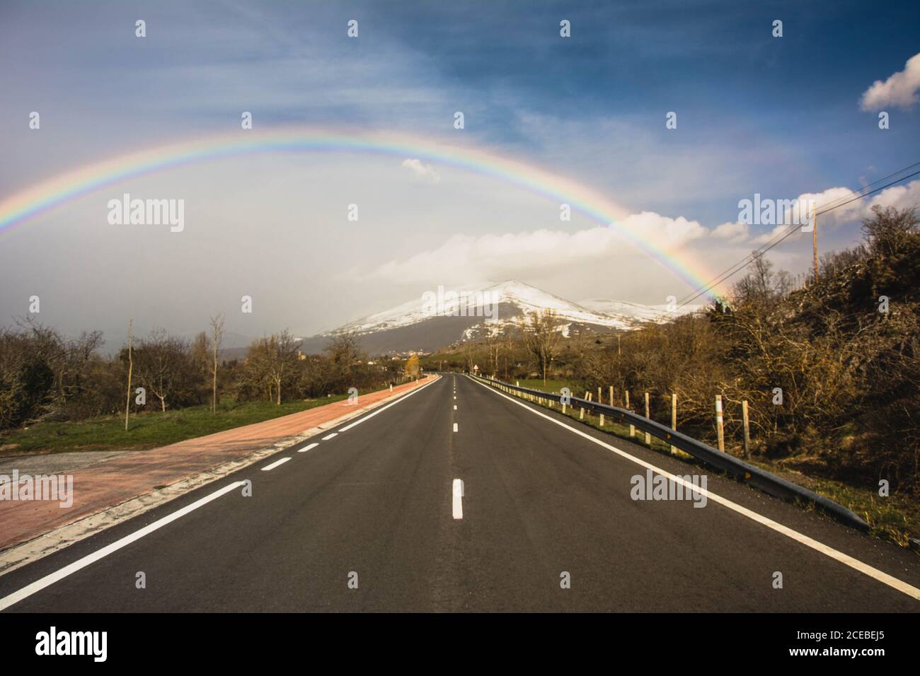 bord de route rural contre les montagnes et l'arc-en-ciel dans le ciel bleu Banque D'Images