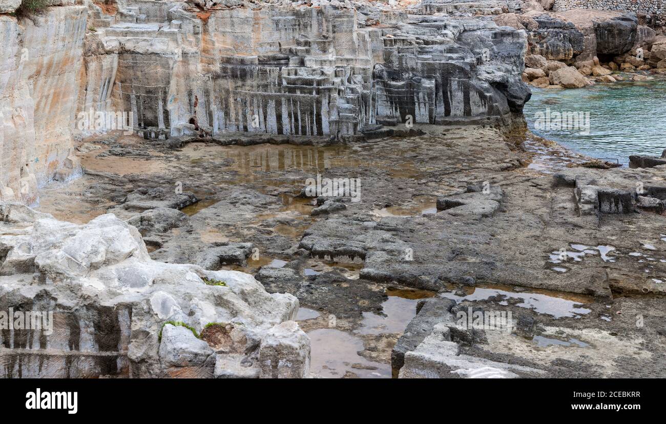 Carrière vieillie avec des murs en pierre rugueuse située près de l'eau calme à Minorque, Espagne Banque D'Images