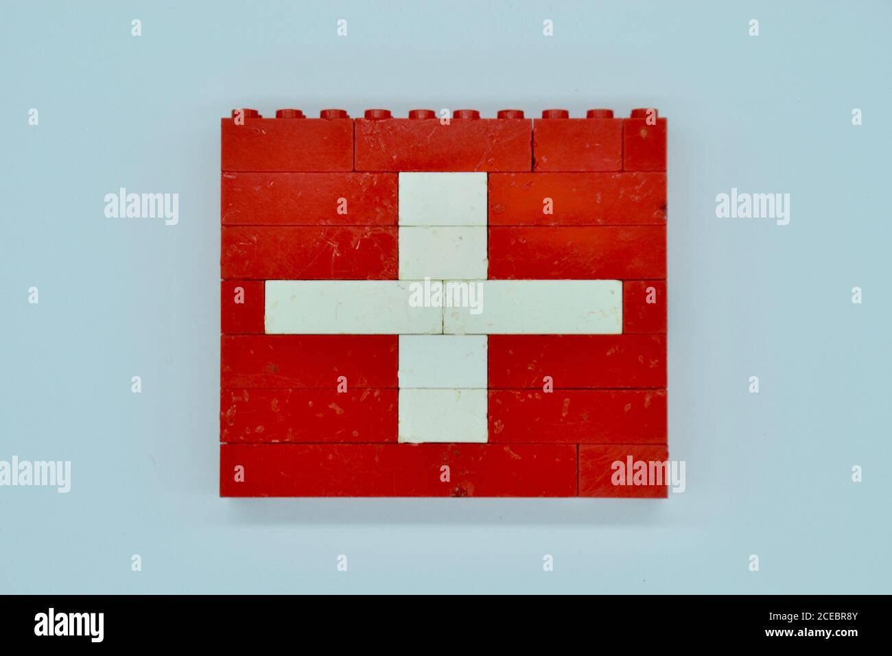 Drapeau national de la Suisse en rouge avec une croix blanche en briques LEGO rétro dans un mur de briques, tourné sur un fond blanc Banque D'Images