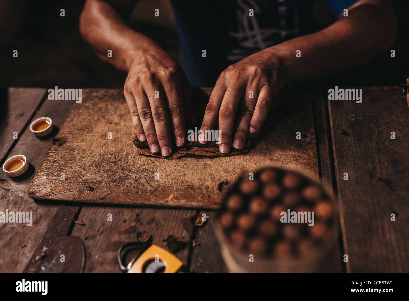 Vue rognée des mains sombres du cigare de l'homme bronzé sur une ancienne table en bois patiné avec des outils autour Banque D'Images Vue rognée des mains sombres du cigare de l'homme bronzé sur une ancienne table en bois patiné avec des outils autour Banque D'Images