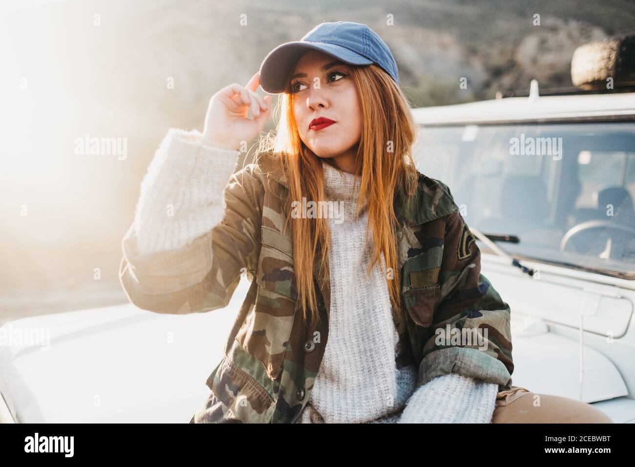 Jeune femme sur une tenue décontractée touchant la casquette et assis sur  la voiture Photo Stock - Alamy
