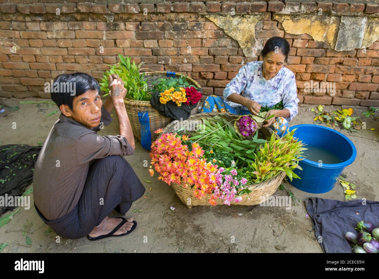 Bagan, Myanmar - juin, 25 2012: D'en haut de l'ethnie homme et femme vendant des fleurs fraîches tout en étant assis près du mur de briques grungy sur la rue de la ville Banque D'Images