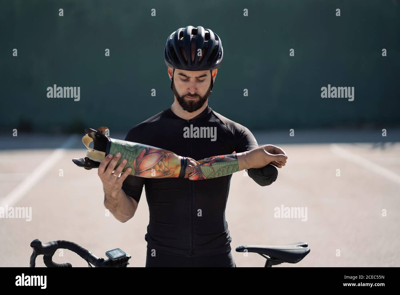 Beau barbu dans un casque tenant une prothèse de bras en se tenant debout près de vélo Banque D'Images