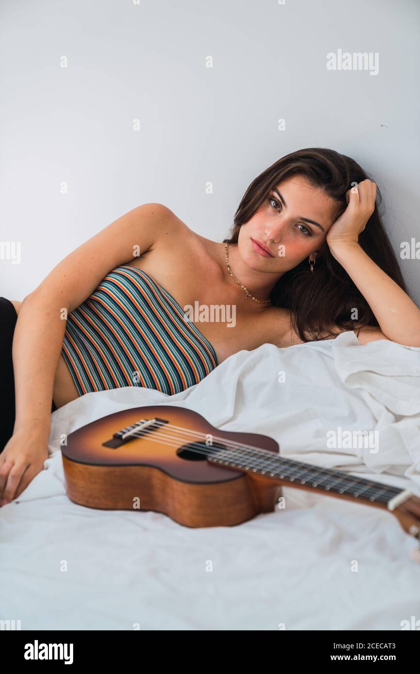 Jeune femme brune couchée au lit avec guitare Banque D'Images