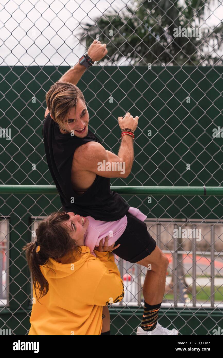 Vue latérale d'une charmante jeune femme qui aide le petit ami à monter une clôture de terrain de sport moderne sur la rue de la ville Banque D'Images